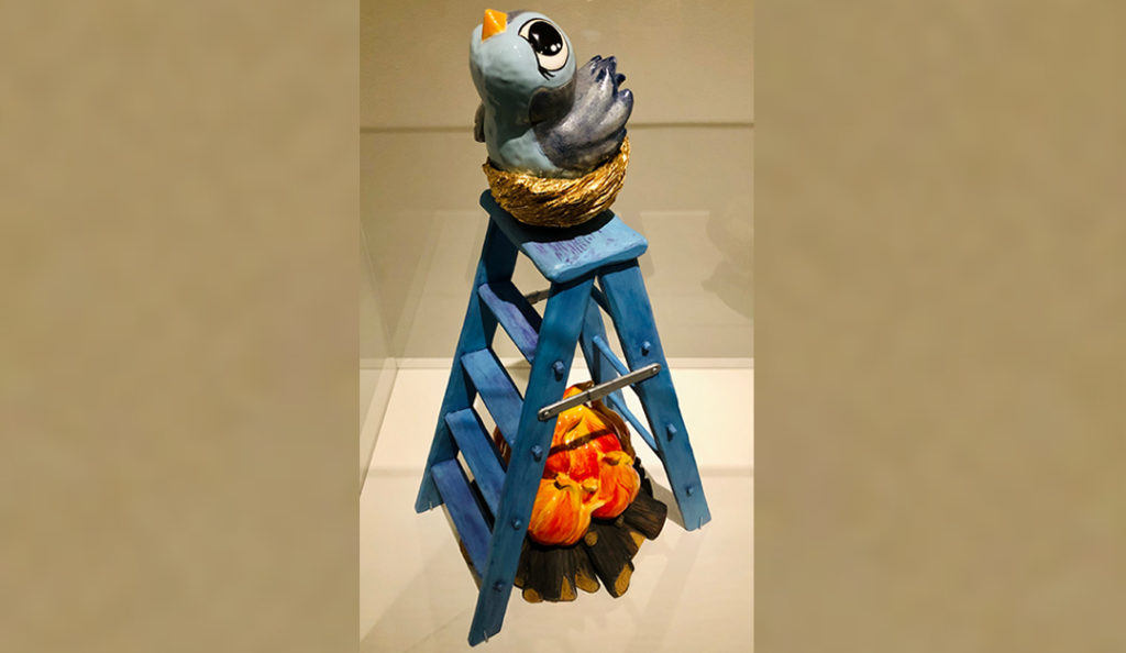 Ceramic sculpture of a bird on top of a ladder by Kristen CliffelI. It is titled, "It Seemed Like a Good Idea at the Time."